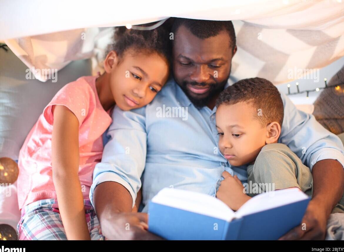 Hombre afroamericano leyendo un cuento antes de dormir a sus hijos en casa...